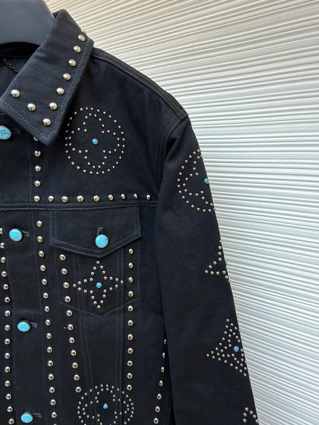 LOUIS VUITTON turquoise rivet denim jacket ●Original version: purchased and developed by 38979 ●Item number: 1682224-E30 ●Material: denim fabric ●Technology: hand-made rivet inlay ●Color: black ●Version: fitted version ●Weight: about 1550 grams ●Size: 46-48-50-52 ●Description: This black denim jacket is made of high-density twill denim fabric and has been treated with pre-washing water. It not only retains the crisp texture of the fabric, but also achieves a soft and skin-friendly wearing experience. The entire body of the garment is made of hand-made rivet inlay technology. The metal rivets are arranged at precise points to outline the outline of the brand's classic logo. Each rivet is manually hammered and fixed to ensure firmness and three-dimensionality. The placket and pockets are decorated with turquoise-textured resin buttons, which contrast with the metal rivets. The stitching on the collar, cuffs and hem adopts a double stitching process to enhance structural stability, while the edges are roughened to add a retro texture. The overall cut is a slightly loose Oversize version, combined with the three-dimensional tailoring process of the three-dimensional shoulder line, taking into account both styling and wearing comfort. Every detail is calibrated by hand, demonstrating the exquisite level of clothing making technology. The overall wiring is straight and delicate, the fabric is comfortable and soft, and the color is consistent without color difference. It can be matched with the same style to create a fashionable look and control various occasions. Customized accessories, complete with three standards, same style for men and women!